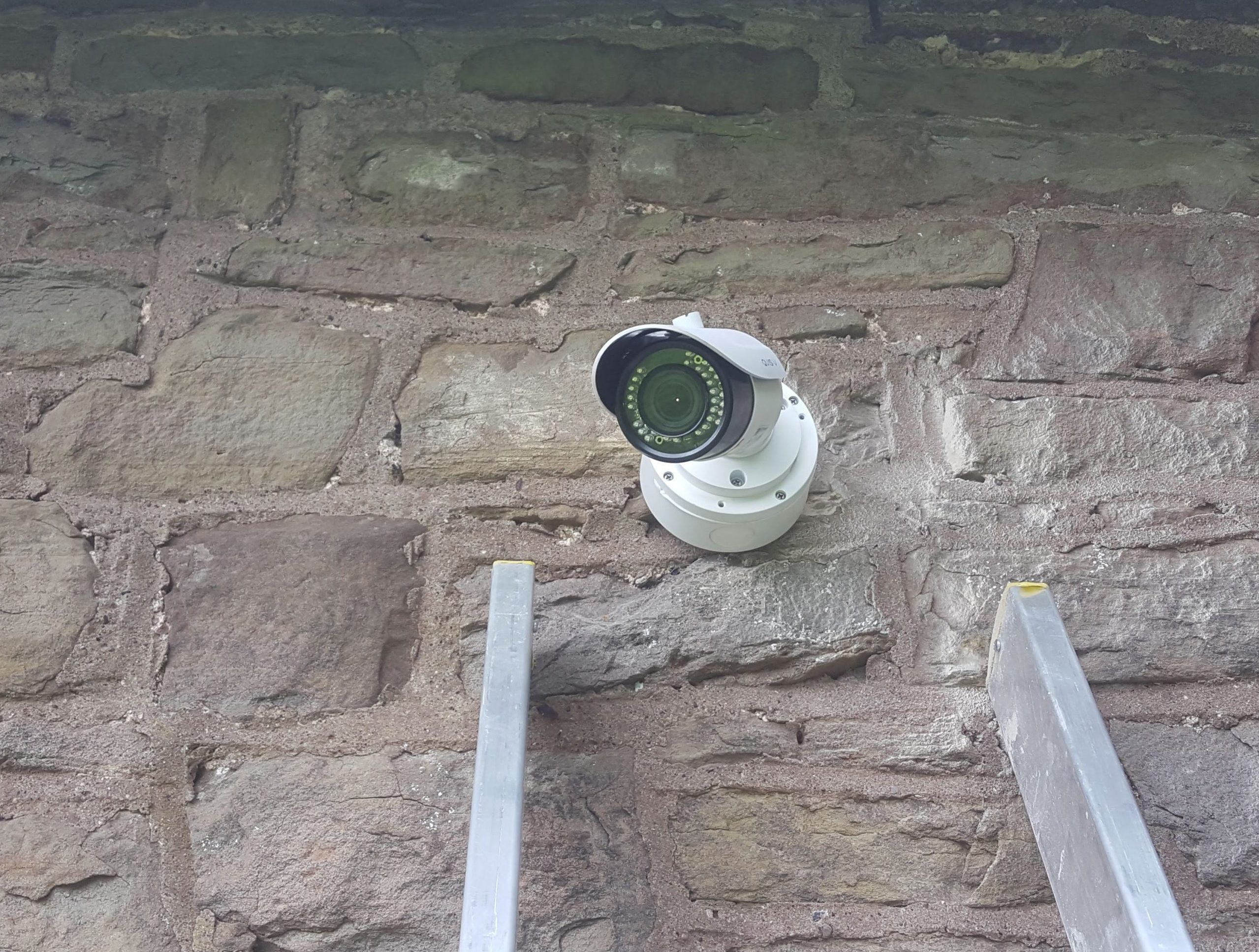 Modern security camera on brick wall with ladder next to it